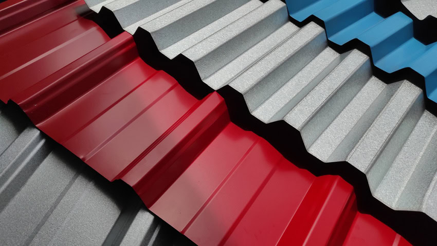 Close-up of overlapping corrugated metal roofing sheets in red, blue, and silver colors, arranged in diagonal rows, showing their wavy, textured patterns and shiny surfaces.